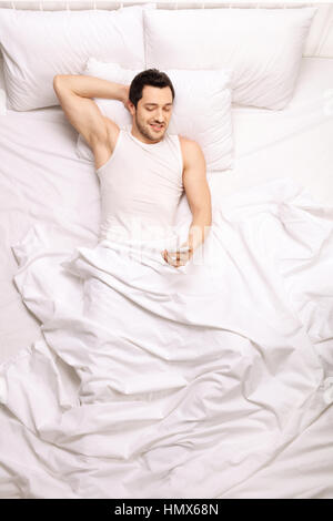 Uomo bello guardando un telefono cellulare mentre giaceva a letto Foto Stock