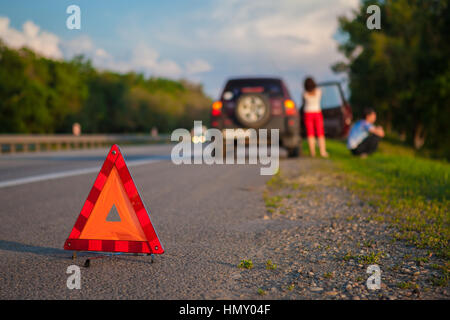 Close-up di un triangolare segno di avvertimento con coppia in piedi di fronte a ripartiti in auto Foto Stock
