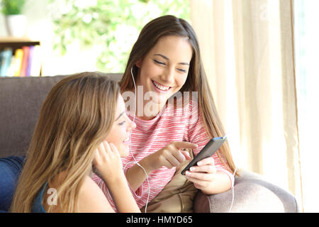 Due amici che ascoltano musica insieme online da smart phone seduta su un divano nel salotto di casa Foto Stock