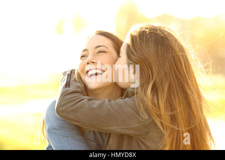 Due amici felice abbracciando e baciando in strada al tramonto con una luce calda Foto Stock