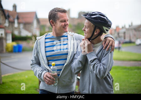 Padre e Figlio tenetevi pronti per il loro giro in bici. Il padre ha il suo braccio intorno a suo figlio ed essi sono sorridente ad ogni altro. Foto Stock