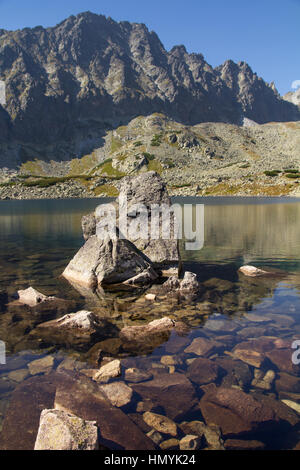 Le rocce in un tranquillo lago di montagna contro lo sfondo di una robusta gamma di montagna che mostra la bellezza del nostro ambiente naturale Foto Stock