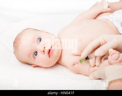 Pediatra dando a tre mesi di baby girl iniezione intramuscolare in braccio. Bambino cerca ansiosamente presso un medico Foto Stock