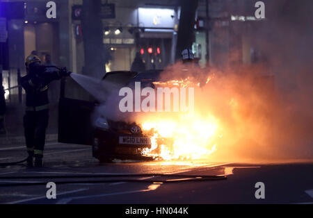 Fire crew mettendo una Toyota Prius che ha preso fuoco in corrispondenza della giunzione di Brompton Road e Brompton Square guardando verso i magazzini Harrods, Londra. Foto Stock