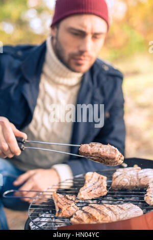 L'uomo la cottura della carne sulla griglia a carbone Foto Stock