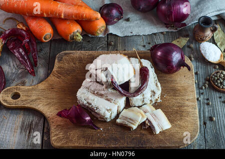 Il sale di pancetta di maiale su una scheda di cucina tra le spezie e verdure, vista dall'alto Foto Stock