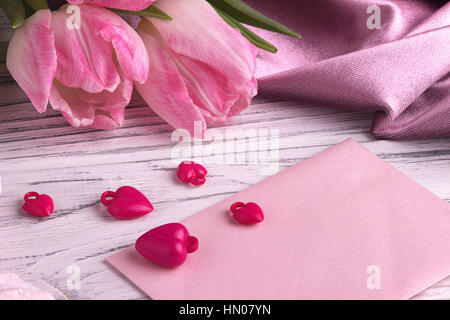 Il giorno di San Valentino con sfondo rosa tulip fiori cuori rossi segno di forma su bianco rosa busta bianca su sfondo di legno.Il giorno di San Valentino. Foto Stock