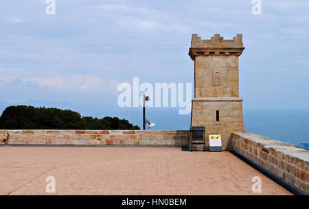 Torre in pietra all'angolo del Castello di Montjuic, Barcellona, con blu sullo sfondo del mare e cielo nuvoloso cielo blu Foto Stock