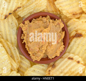 Top vista ravvicinata di una piccola ciotola di hummus salsa di carciofi con patate fritte che circonda il recipiente su una piastra. Foto Stock