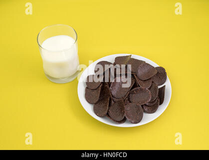 Una piastra di cioccolato scuro coperto rice crisp wafer con un bicchiere di latte al lato sulla cima di una tovaglia di colore giallo. Foto Stock
