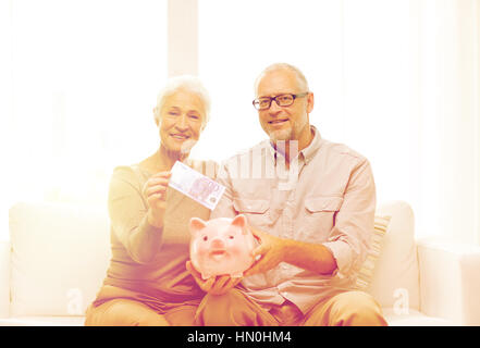 Coppia senior con il denaro e il salvadanaio a casa Foto Stock