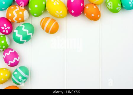 Coloratissimo uovo di pasqua angolo bordo contro un bianco sullo sfondo di legno Foto Stock