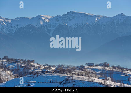 Paesaggio rurale con un tradizionale villaggio rumeno alla base delle montagne di Bucegi su un soleggiato freddo inverno mattina in Pestera, Brasov county, Transylvan Foto Stock