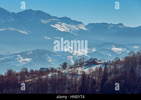 Inverno idilliaco paesaggio rurale con rustici Romanian case nel villaggio di Pestera, nella valle di montagne di Bucegi, Transilvania regione, Romania. Foto Stock