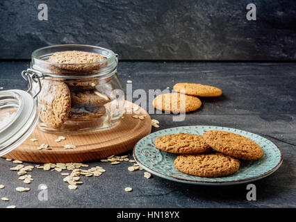 I cookies di avena giaceva su una piastra e banca con i fiocchi d'avena i cookie in piedi su una tavola di legno. Foto Stock