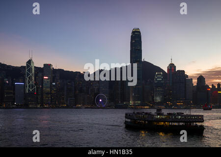 Silhouette di una Star Ferry e grattacieli illuminati al distretto centrale dell'Isola di Hong Kong in Hong Kong, Cina, al tramonto. Vista da Tsim Sha Tsui. Foto Stock