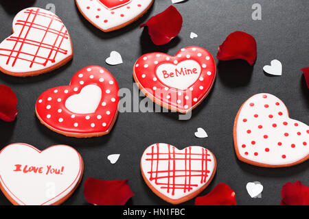 Bella gingerbread cuore rosso e petali di rose su uno sfondo nero. Cartolina per il giorno di San Valentino, 8 Marzo Giornata della madre o di un matrimonio. Foto Stock