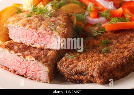 Scamone bistecca nel pangrattato e guarnito con verdure su di una piastra orizzontale di macro Foto Stock