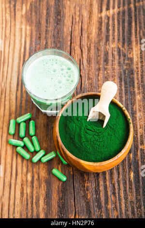 Spirulina in polvere nella ciotola di legno con spirulina pillole e verde bicchiere per frullato Foto Stock