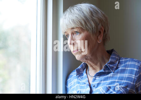 Senior donna che soffre di depressione guardando fuori della finestra Foto Stock