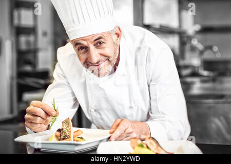 Primo piano della sorridente chef maschio la farcitura di prodotti alimentari in cucina Foto Stock