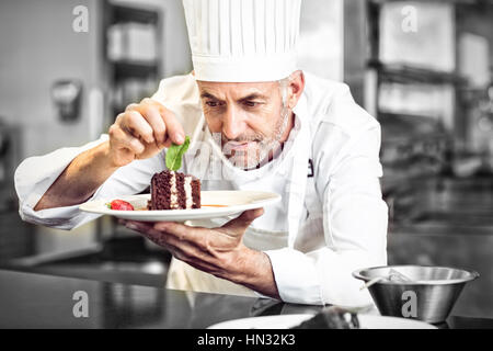 Primo piano di un maschio di concentrato pasticcere decorare il dessert in cucina Foto Stock