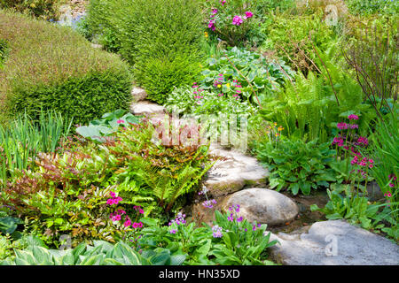 Pietre miliari fra verdi hosta, felci fiori colorati, arbusti, in un estate English Garden cottage Foto Stock