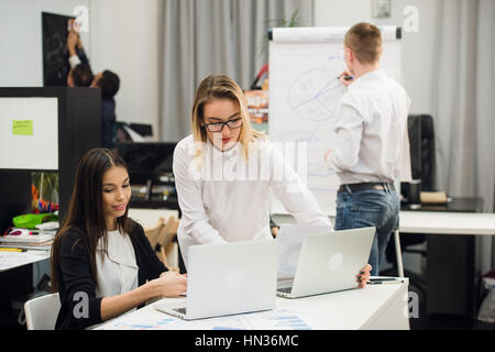 Due belle office i lavoratori aventi la conversazione mentre l uomo collega il disegno della strategia aziendale sulla lavagna a fogli mobili. Foto Stock