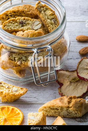 Gustosi e sani biscotti di mandorle, ricco di vitamine e minerali in un vasetto di vetro e le mandorle e secche Mele secche limoni su un bianco tavolo di legno. Chiudere u Foto Stock