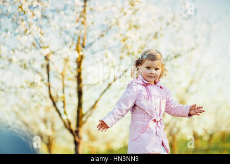 Piccola bambina di 3 anni che corre tra alberi fioriti outd Foto Stock