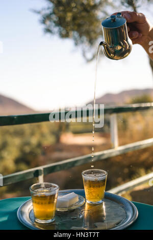 Una mano che tiene una teiera e prepara un tè alla menta come viene fatto in Marocco. Foto Stock