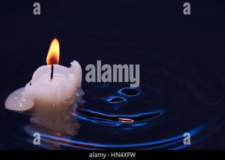 Illuminazione di una candela nel buio di spruzzi di superficie di acqua Foto Stock