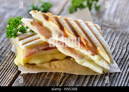 Premuto e tostare panini doppia con prosciutto e formaggio servita su carta a sandwich su un tavolo di legno Foto Stock