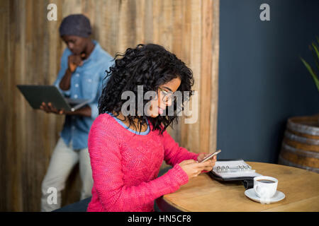 Donna seduta a tavola e utilizzando il telefono cellulare mentre avente un caffè in cafÃƒÂ© Foto Stock