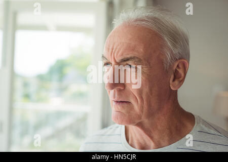 Riflessivo senior uomo in piedi accanto alla finestra a casa Foto Stock