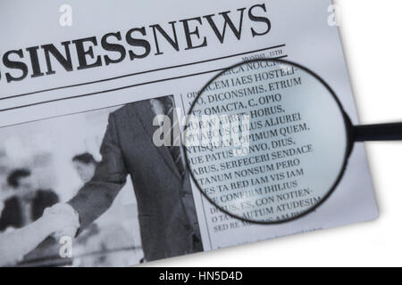 Close-up di lente di ingrandimento sulla carta da giornale contro uno sfondo bianco Foto Stock