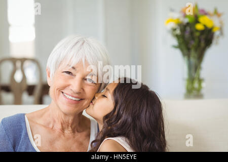 Nipote di baciare la nonna sulla guancia nel salotto di casa Foto Stock