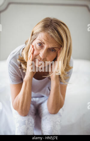 Ritratto di teso donna seduta sul letto in camera da letto a casa Foto Stock