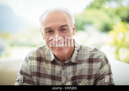 Ritratto di sorridere senior uomo seduto sul divano nel soggiorno di casa Foto Stock