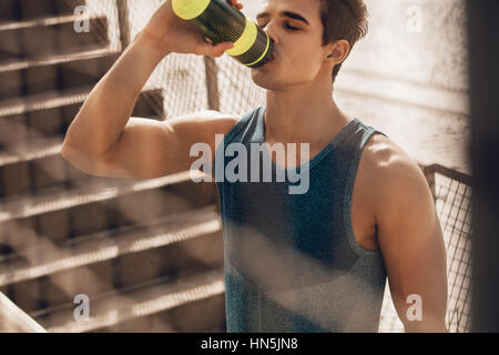 Colpo di muscolare di giovane uomo acqua potabile dalla spiaggia dopo l'allenamento. Runner acqua potabile dopo esercizio e tenendo in pausa. Foto Stock