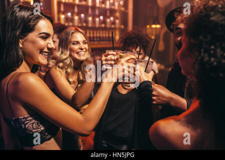 Un gruppo di giovani con i cocktail al night club. Migliori amici partying in un pub e tostatura di bevande. Foto Stock