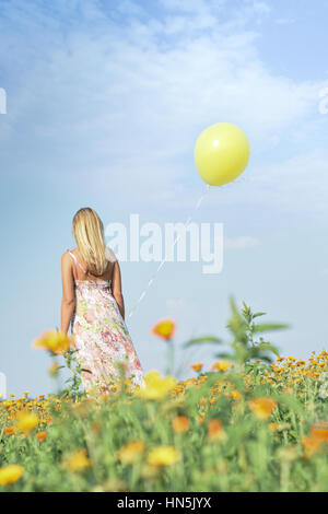 Ragazza in abiti colorati visitatore occasionale con giallo palloncino attraverso un campo in una giornata di sole. Foto Stock