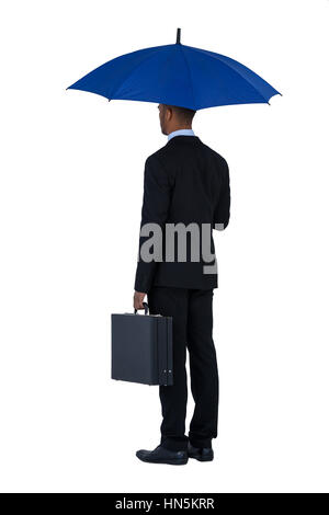 Vista posteriore del businessman holding ombrello blu e una valigetta contro uno sfondo bianco Foto Stock