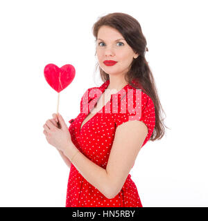 Bella donna in abito rosso rosso di contenimento a forma di cuore lecca-lecca di fronte il suo isolato su bianco Foto Stock