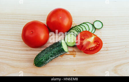 Fette di pomodori e cetrioli su tavola di legno. Foto Stock