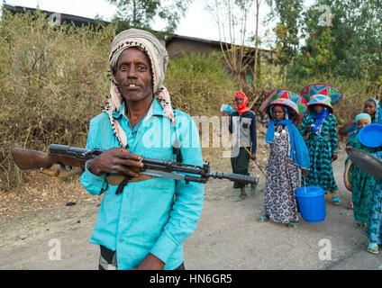 Uomo etiope con una pistola e donne che portano doni durante un matrimonio Oromo celebrazione, Amhara Region, Artuma, Etiopia Foto Stock