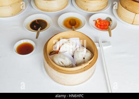 Dim sum il cibo cotto a vapore carne di maiale barbecue bun nel cestello di bambù al ristorante con la salsa di soia salsa dolce, salsa chili e bastoncini. Foto Stock