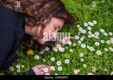 Profilo Ritratto di giovane ragazza distesa in un letto di Daisy bianca camomilla fiori selvaggi e tarassaco sorridente e maleodoranti in erba Foto Stock