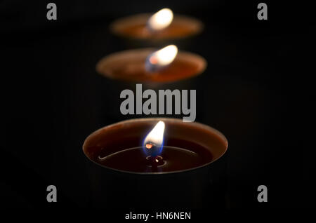 Primo piano di tre luci di tè incandescente al buio con cera rossa e la fiamma Foto Stock