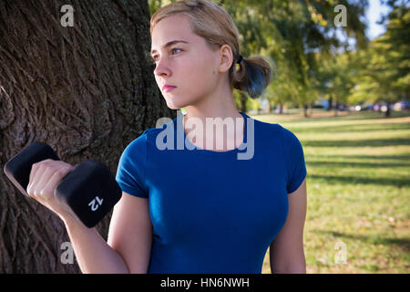 Montare la giovane donna facendo 12 pound dumbbell curl nel verde parco all'aperto Foto Stock